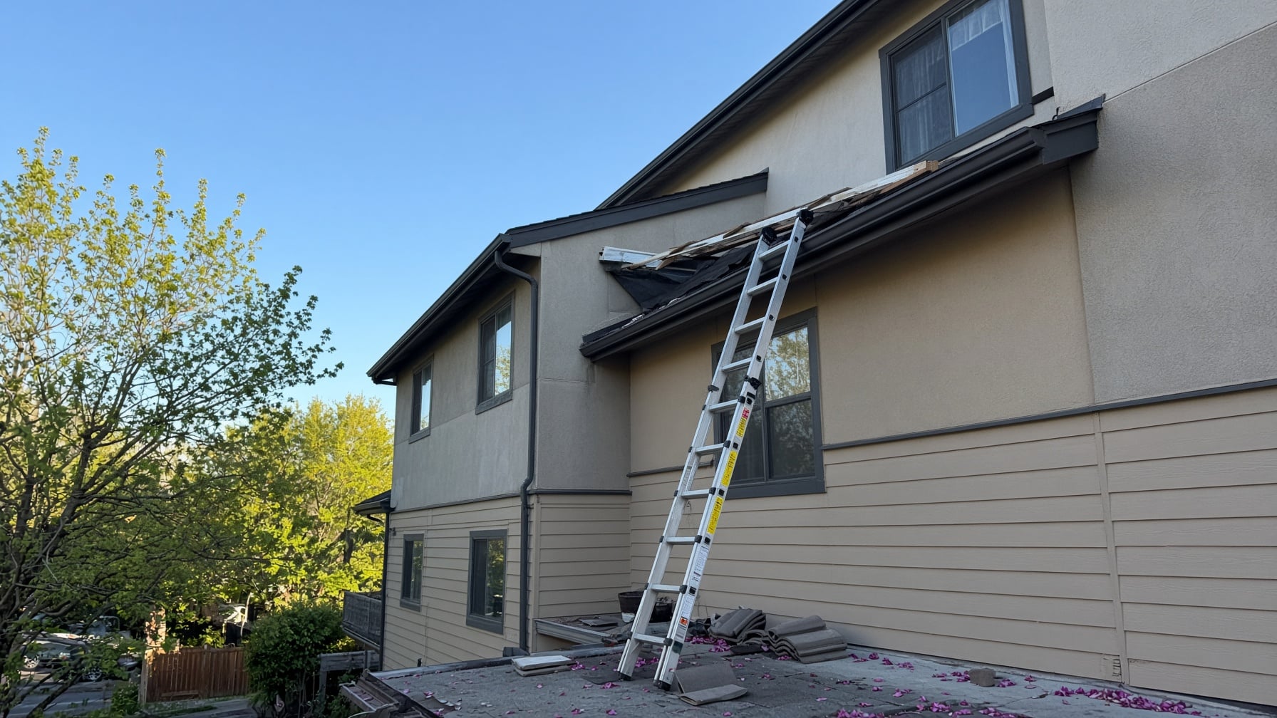 An extension ladder leans against the side of a house, reaching toward a damaged section of the roof where shingles are missing, a property repair overseen by SLPM association management services.